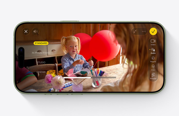 iPhone 17 mostrato di fronte, funzione Mix audio in uso nel video di una bambina che gioca seduta a un tavolo con palloncini sullo sfondo