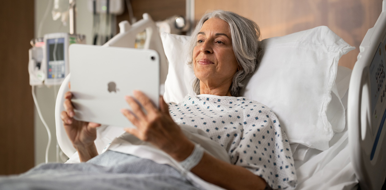一位女病人躺在病床上看著 iPad。